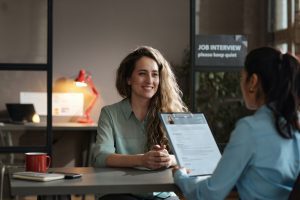Young woman sitting at table and smiling while manager examining her resume during job interview.